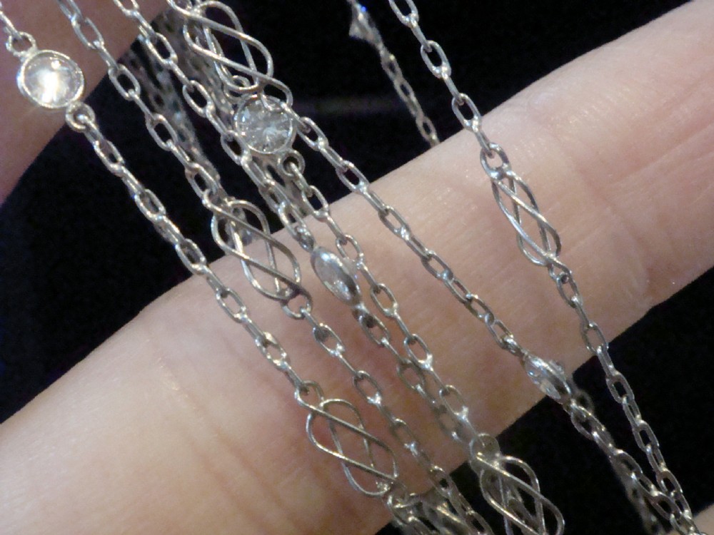 An Edwardian 18ct white gold longuard chain featuring spectacle-set round diamonds interspersed with delicate open wirework links.