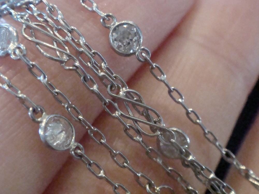 An Edwardian 18ct white gold longuard chain featuring spectacle-set round diamonds interspersed with delicate open wirework links. View II