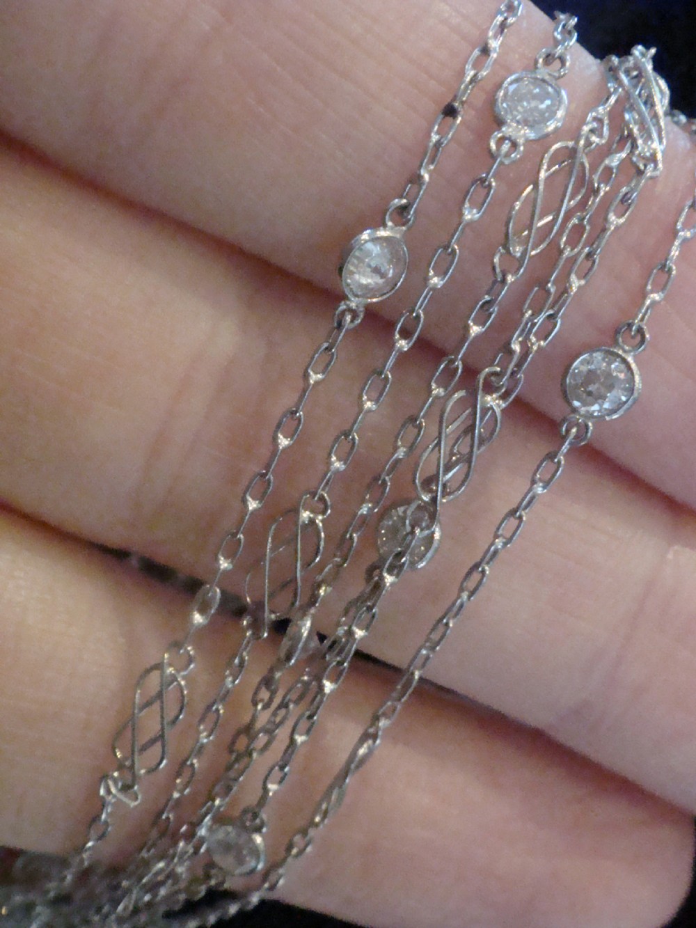 An Edwardian 18ct white gold longuard chain featuring spectacle-set round diamonds interspersed with delicate open wirework links. View V