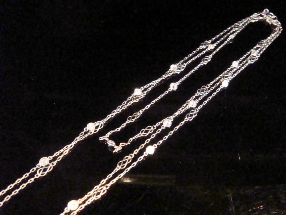 An Edwardian 18ct white gold longuard chain featuring spectacle-set round diamonds interspersed with delicate open wirework links. View VI