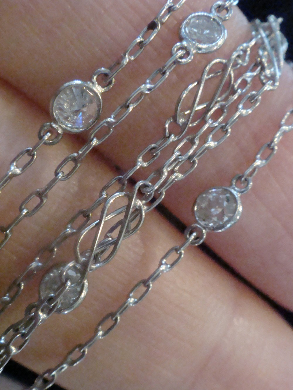 An Edwardian 18ct white gold longuard chain featuring spectacle-set round diamonds interspersed with delicate open wirework links. View VII