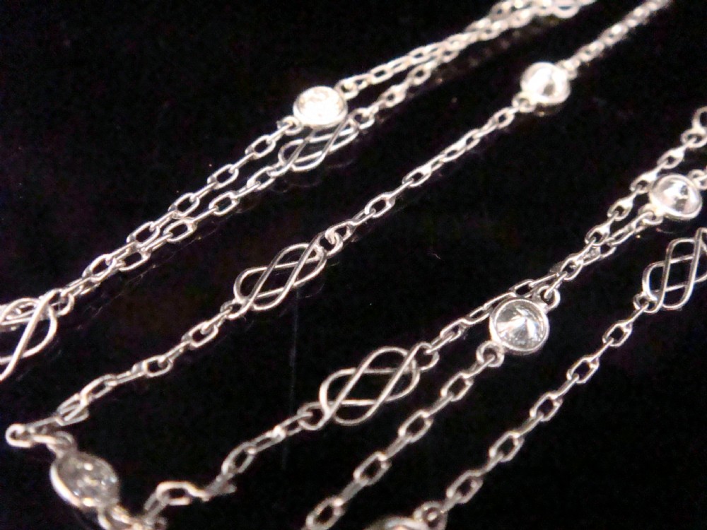 An Edwardian 18ct white gold longuard chain featuring spectacle-set round diamonds interspersed with delicate open wirework links. View VIII