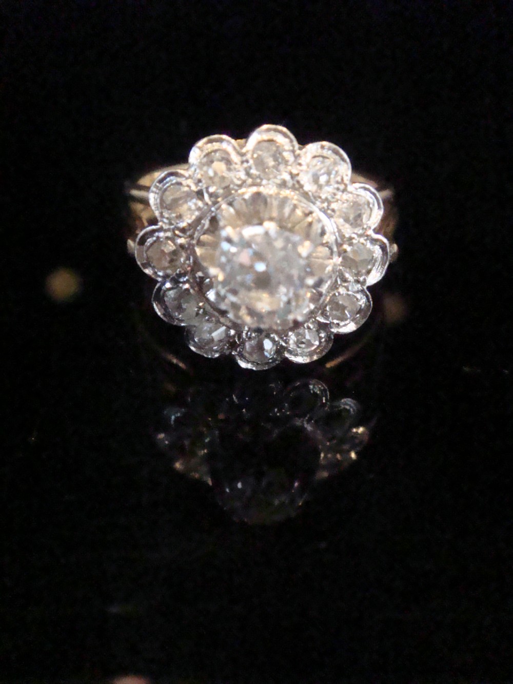 An Edwardian 18ct yellow gold cluster ring set with a central old-cut diamond surrounded by a floral halo of smaller old-cut diamonds.