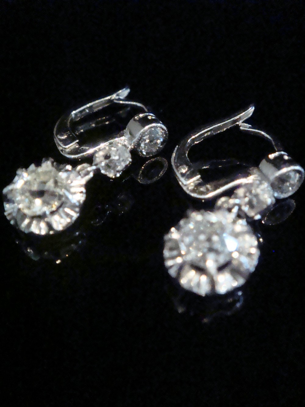 A pair of Edwardian 18ct white gold drop earrings featuring circular old cut diamond clusters suspended from lever-back fittings.