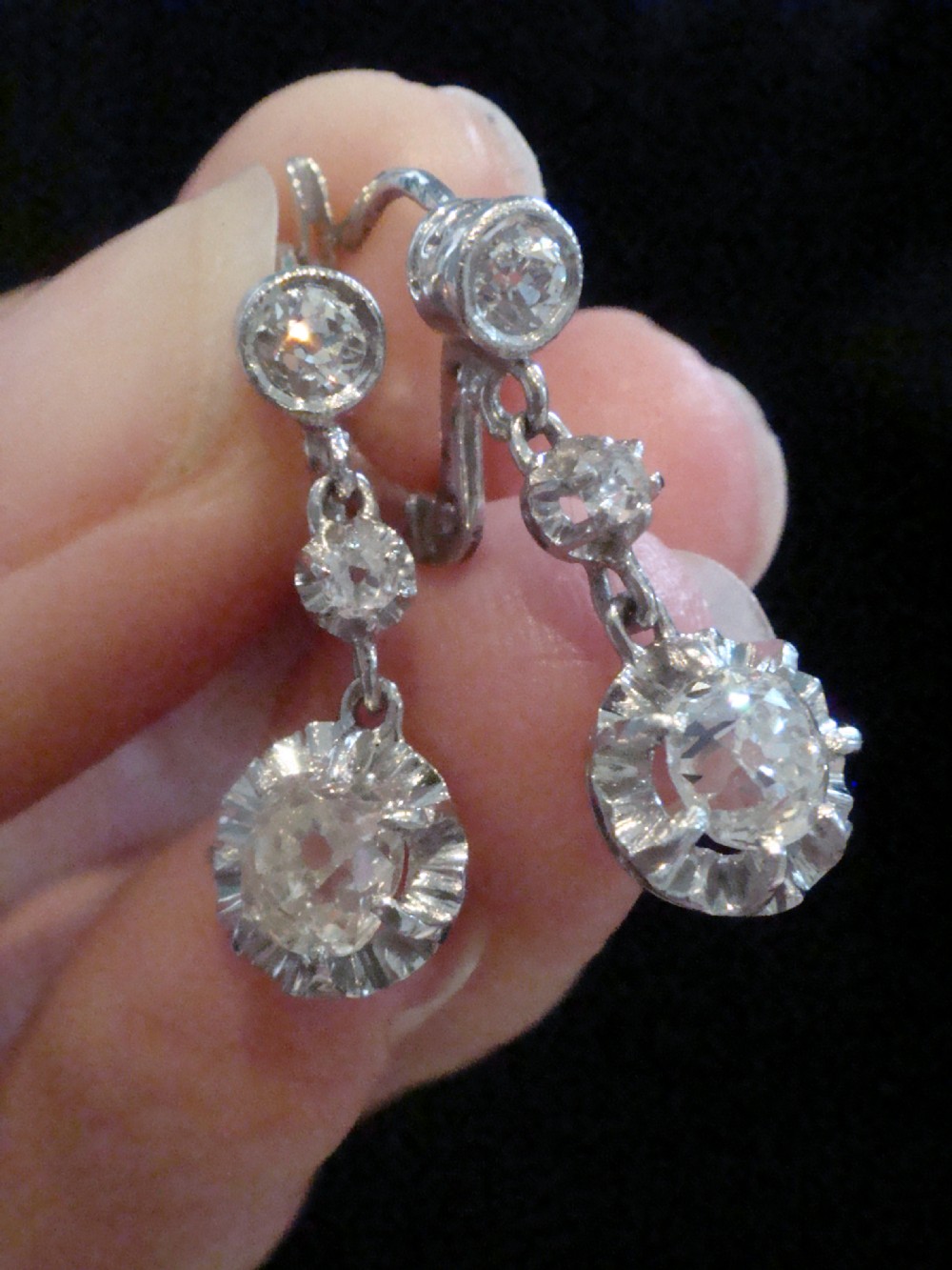 A pair of Edwardian 18ct white gold drop earrings featuring circular old cut diamond clusters suspended from lever-back fittings. View II