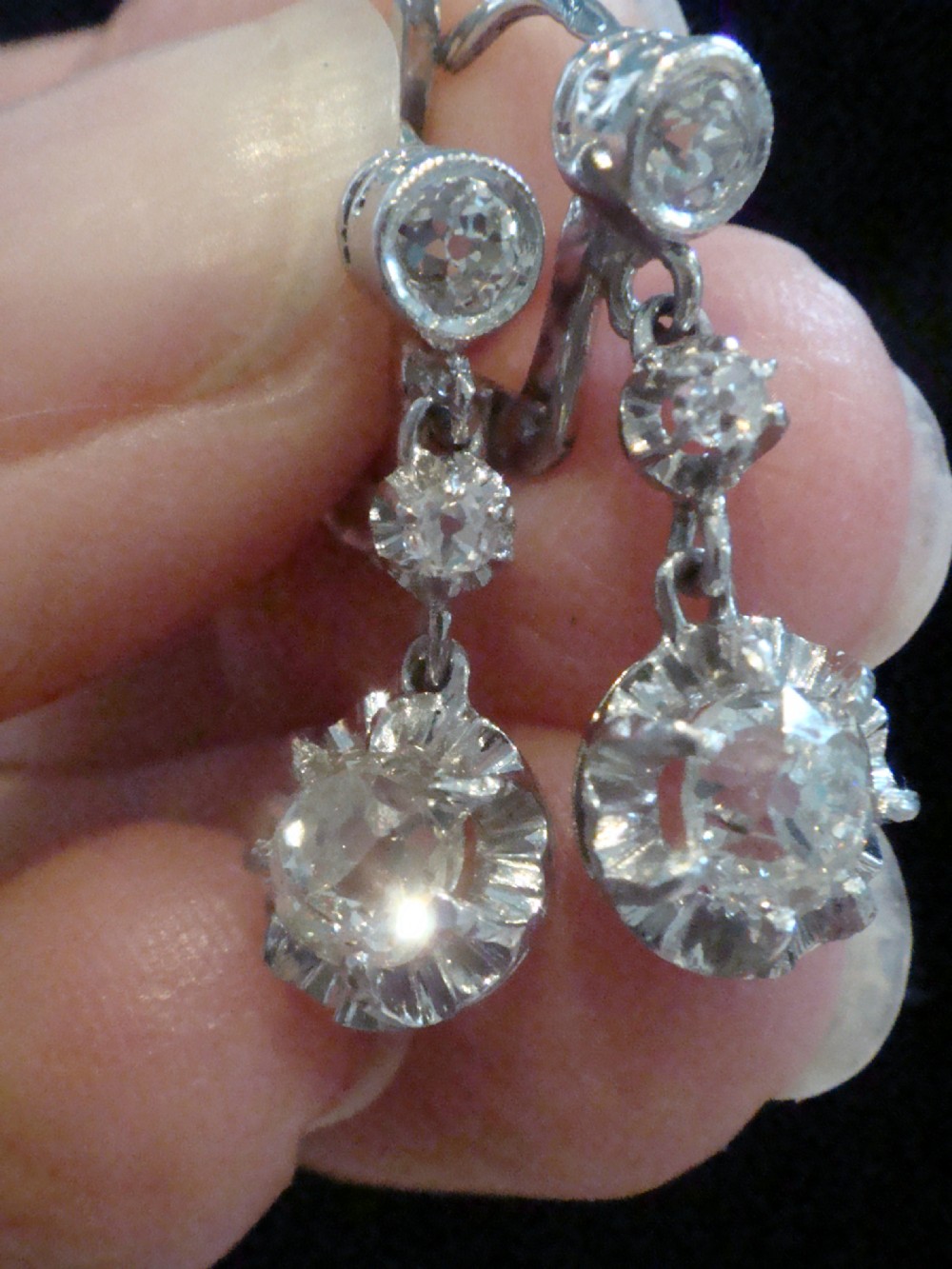 A pair of Edwardian 18ct white gold drop earrings featuring circular old cut diamond clusters suspended from lever-back fittings. View III
