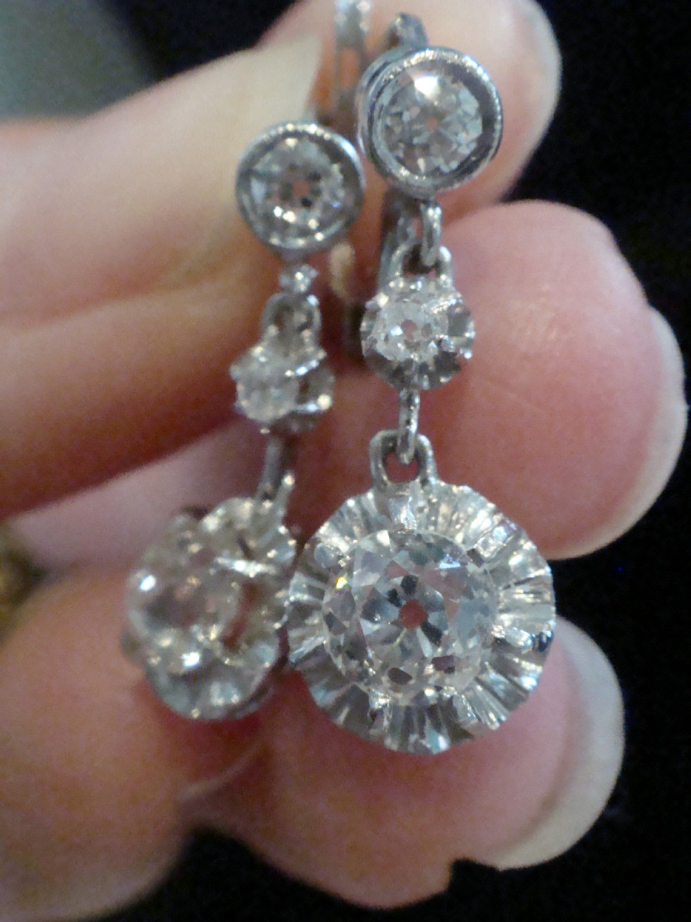 A pair of Edwardian 18ct white gold drop earrings featuring circular old cut diamond clusters suspended from lever-back fittings. View IV