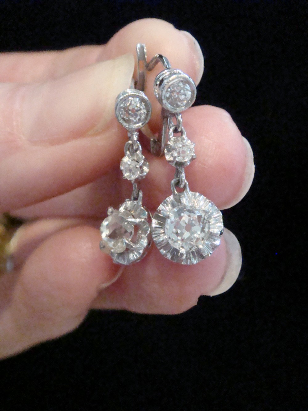 A pair of Edwardian 18ct white gold drop earrings featuring circular old cut diamond clusters suspended from lever-back fittings. View V
