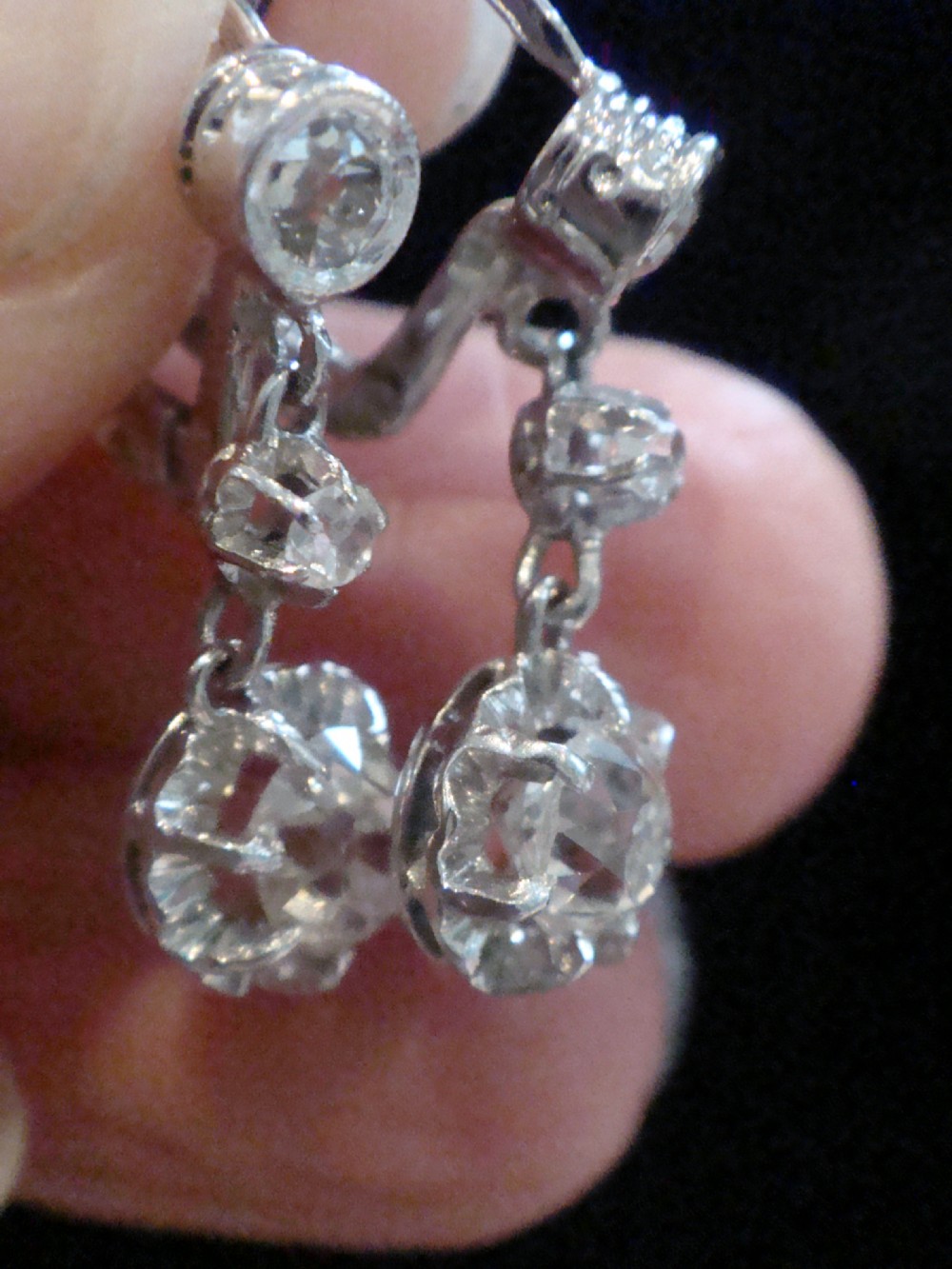 A pair of Edwardian 18ct white gold drop earrings featuring circular old cut diamond clusters suspended from lever-back fittings. View VI