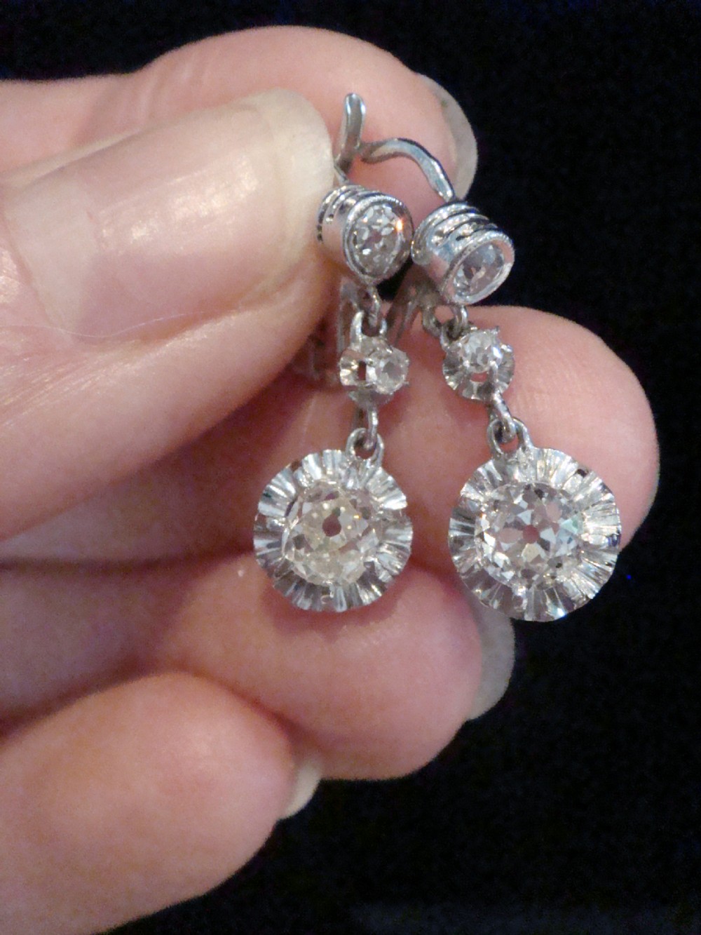 A pair of Edwardian 18ct white gold drop earrings featuring circular old cut diamond clusters suspended from lever-back fittings. View VII