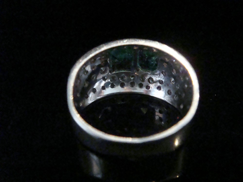 A wide 18ct white gold Retro tank ring featuring two emerald-cut green emeralds set at the centre, surrounded by pave-set round diamonds. View III