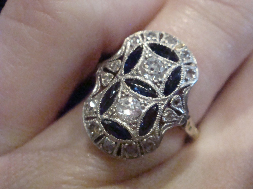 An antique Art Deco plaque ring featuring central diamonds and geometric blue sapphires set with millegrain edging on a gold band.