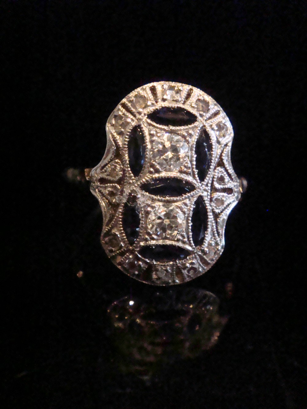 An antique Art Deco plaque ring featuring central diamonds and geometric blue sapphires set with millegrain edging on a gold band. View II