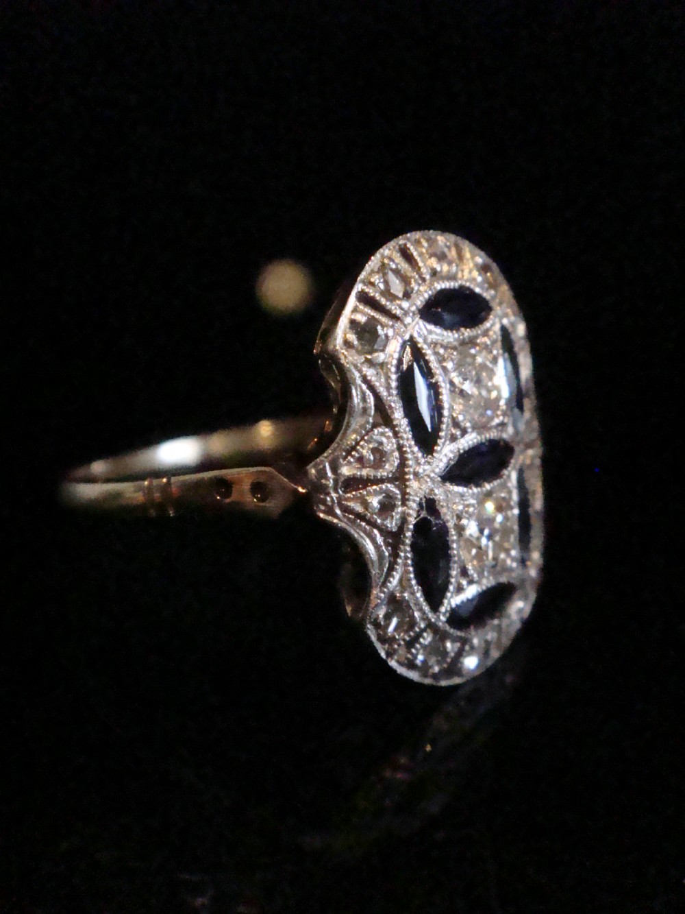 An antique Art Deco plaque ring featuring central diamonds and geometric blue sapphires set with millegrain edging on a gold band. View III