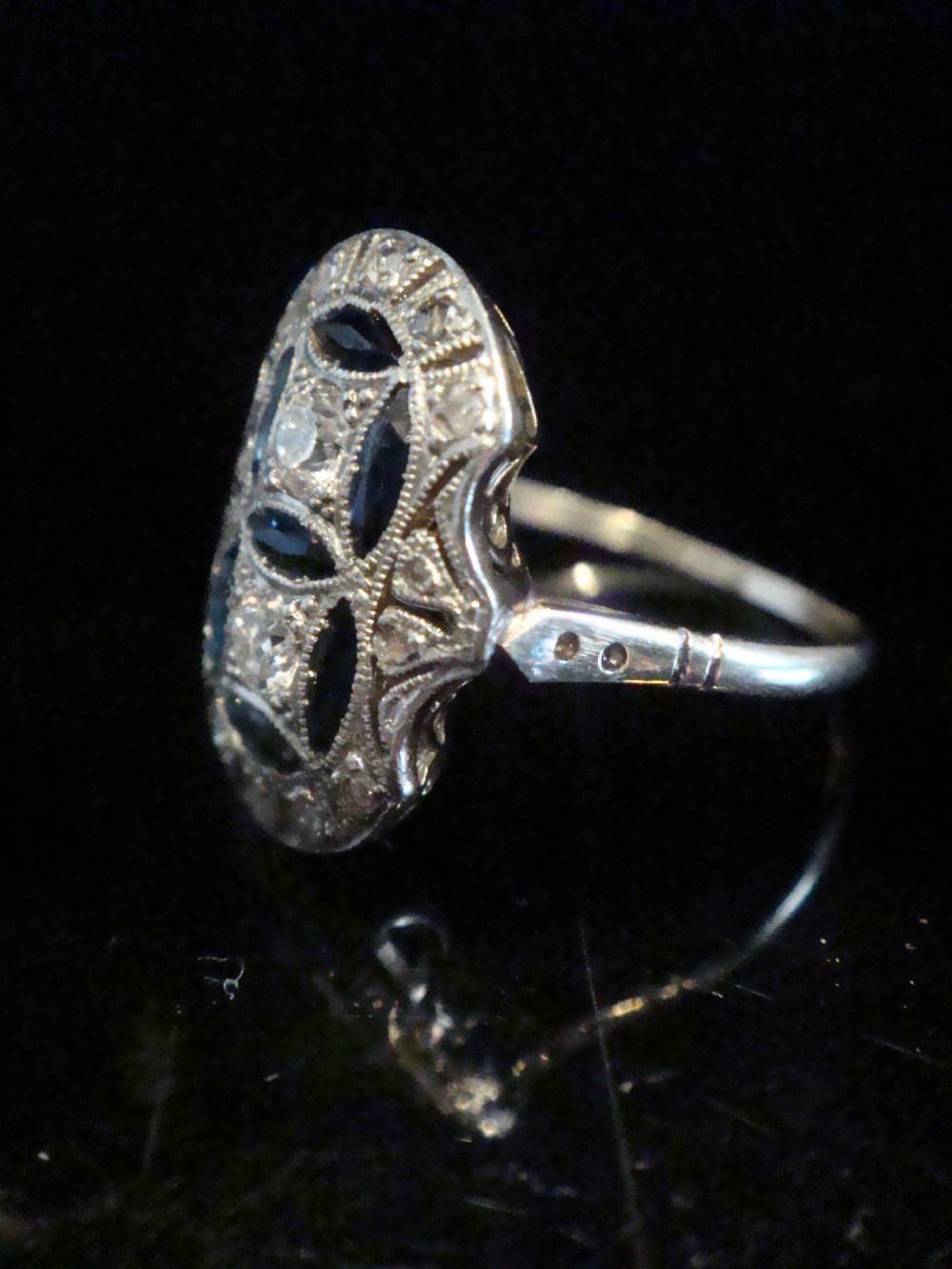 An antique Art Deco plaque ring featuring central diamonds and geometric blue sapphires set with millegrain edging on a gold band. View IV