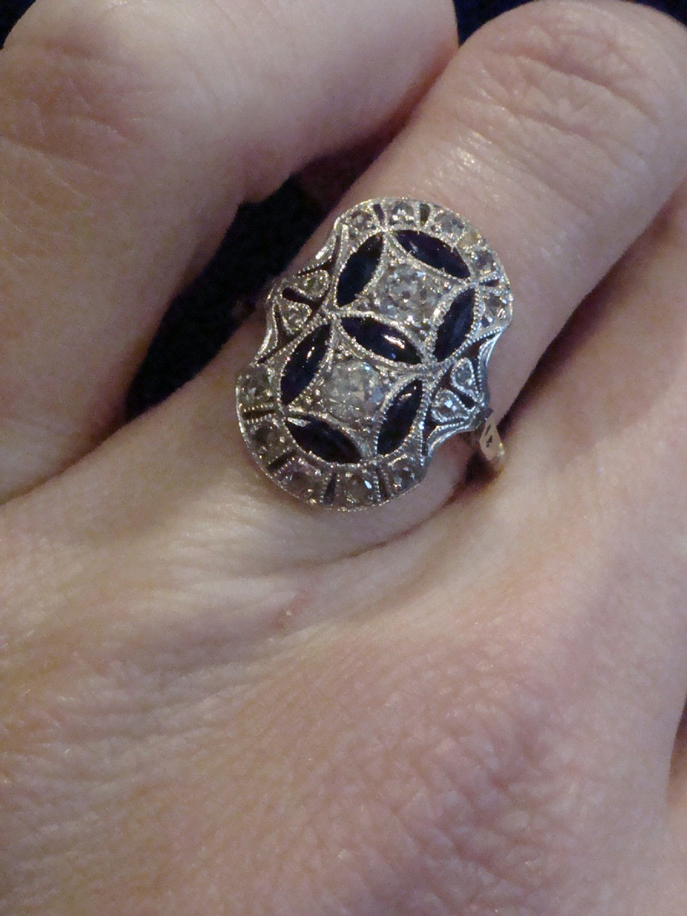 An antique Art Deco plaque ring featuring central diamonds and geometric blue sapphires set with millegrain edging on a gold band. View V