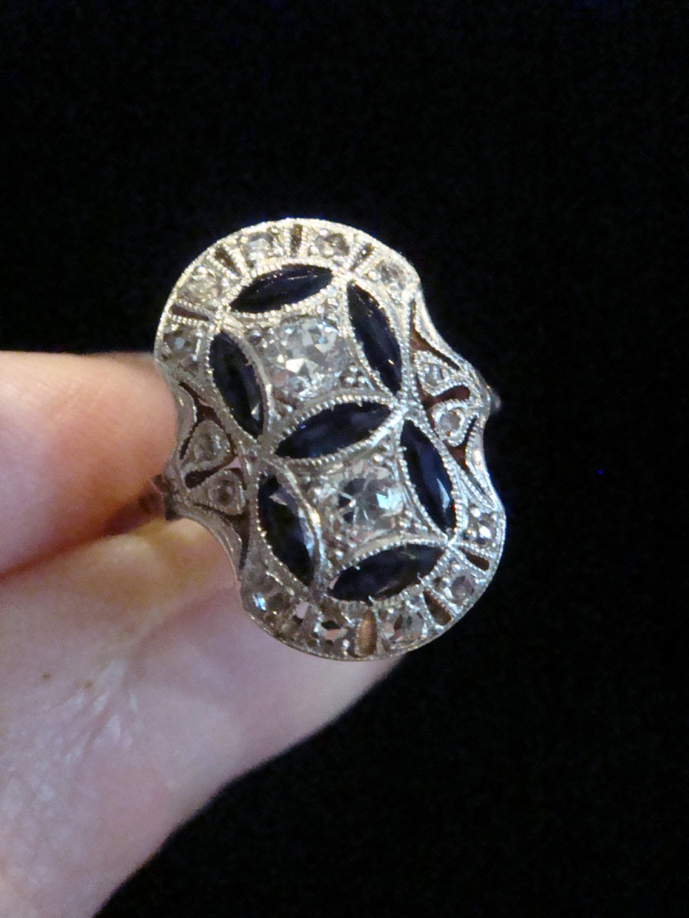 An antique Art Deco plaque ring featuring central diamonds and geometric blue sapphires set with millegrain edging on a gold band. View VI