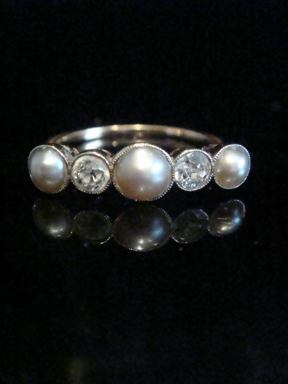 An Edwardian 18ct gold five-stone ring featuring three graduated pearls interspersed with two round diamonds in bezel settings.