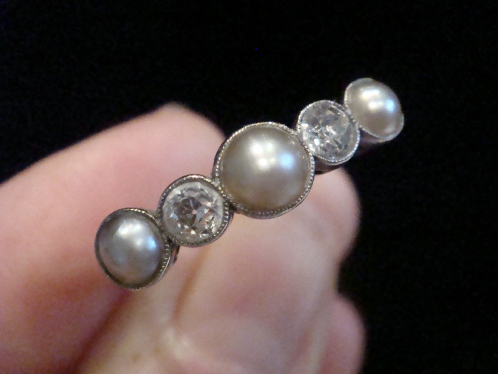 An Edwardian 18ct gold five-stone ring featuring three graduated pearls interspersed with two round diamonds in bezel settings. View IV
