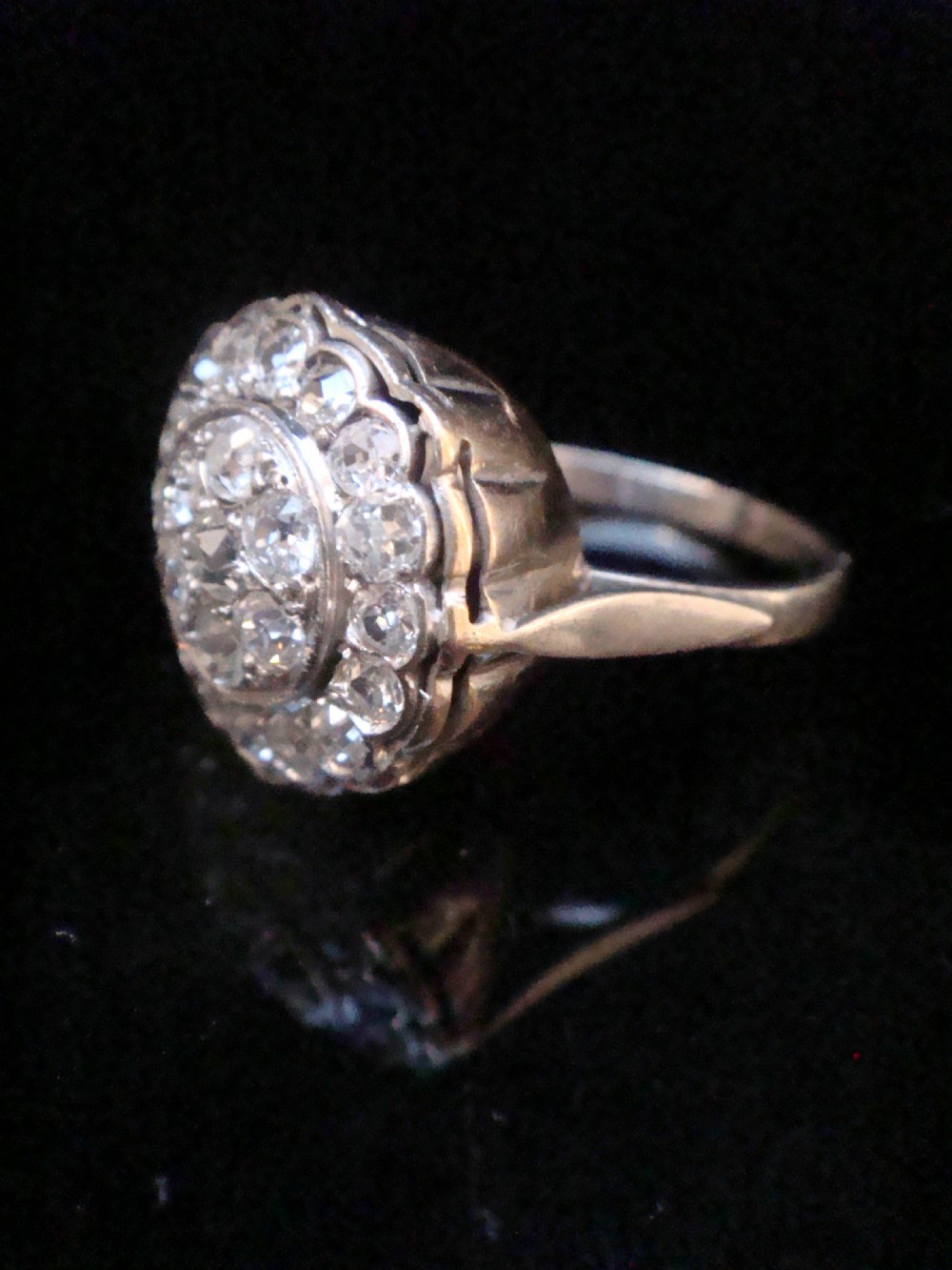 A circular 18ct white gold Edwardian cluster ring set with multiple old cut diamonds featuring a scalloped edge. View II