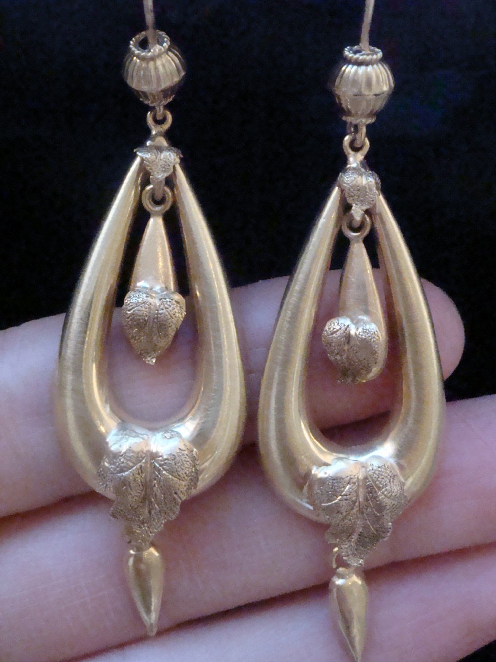 A pair of Victorian 9ct yellow gold drop earrings featuring open teardrop frames embellished with detailed leaf motifs and hanging lower drops. View II