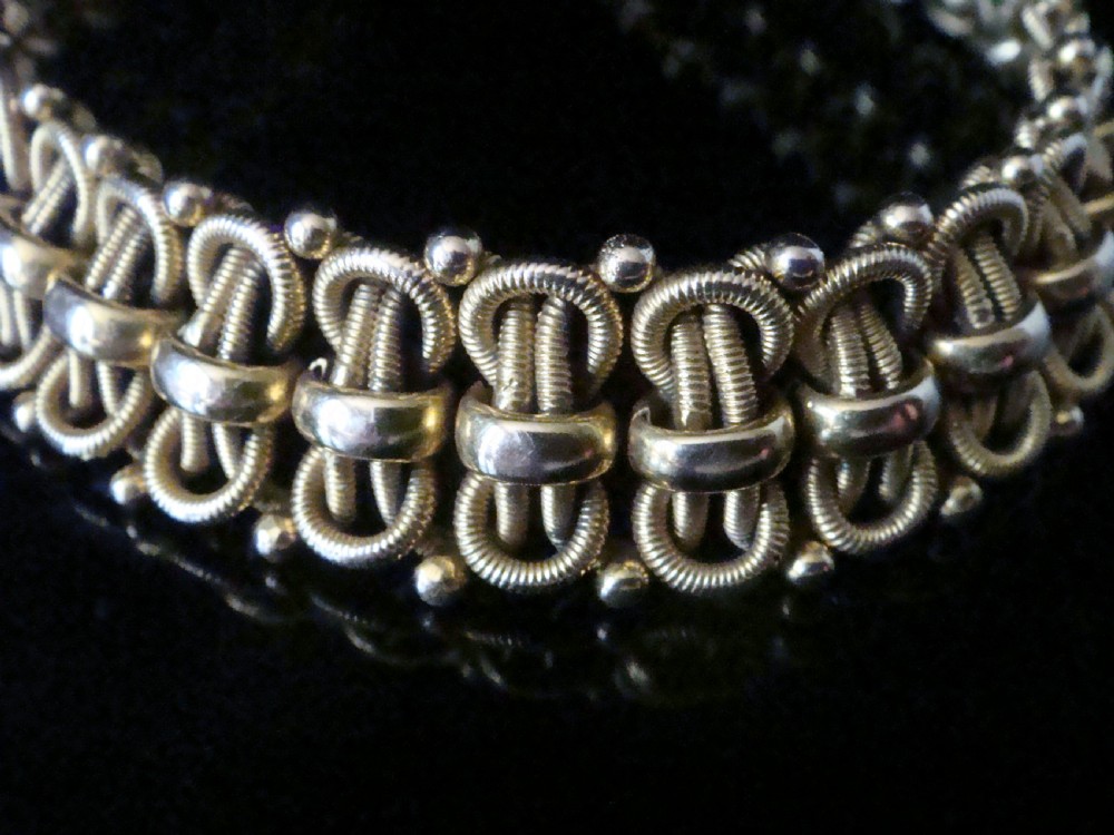 An Edwardian 18ct yellow gold bracelet featuring intricate interlocking wirework links and granulated bead detailing. View V