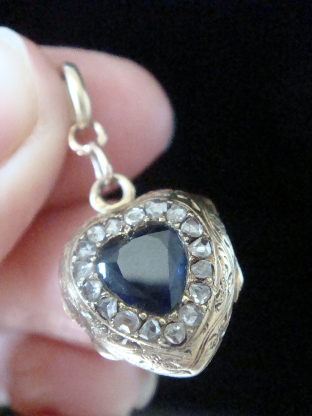 A heart-shaped 18ct gold Edwardian locket set with a central blue sapphire framed by small diamonds and detailed edge engraving. View III