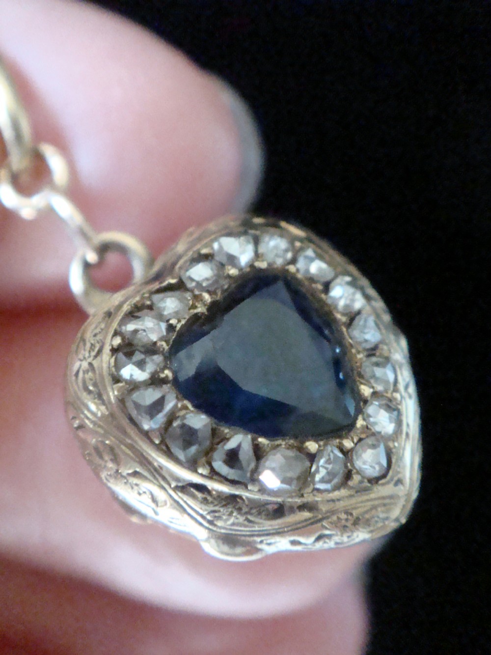 A heart-shaped 18ct gold Edwardian locket set with a central blue sapphire framed by small diamonds and detailed edge engraving. View IV