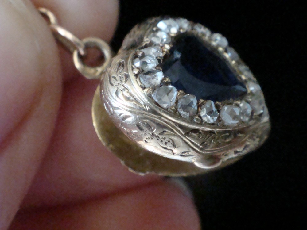 A heart-shaped 18ct gold Edwardian locket set with a central blue sapphire framed by small diamonds and detailed edge engraving. View VII