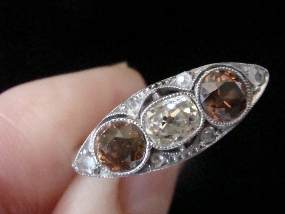 An antique platinum ring featuring a central round white diamond flanked by two natural brown diamonds with millegrain borders. View II