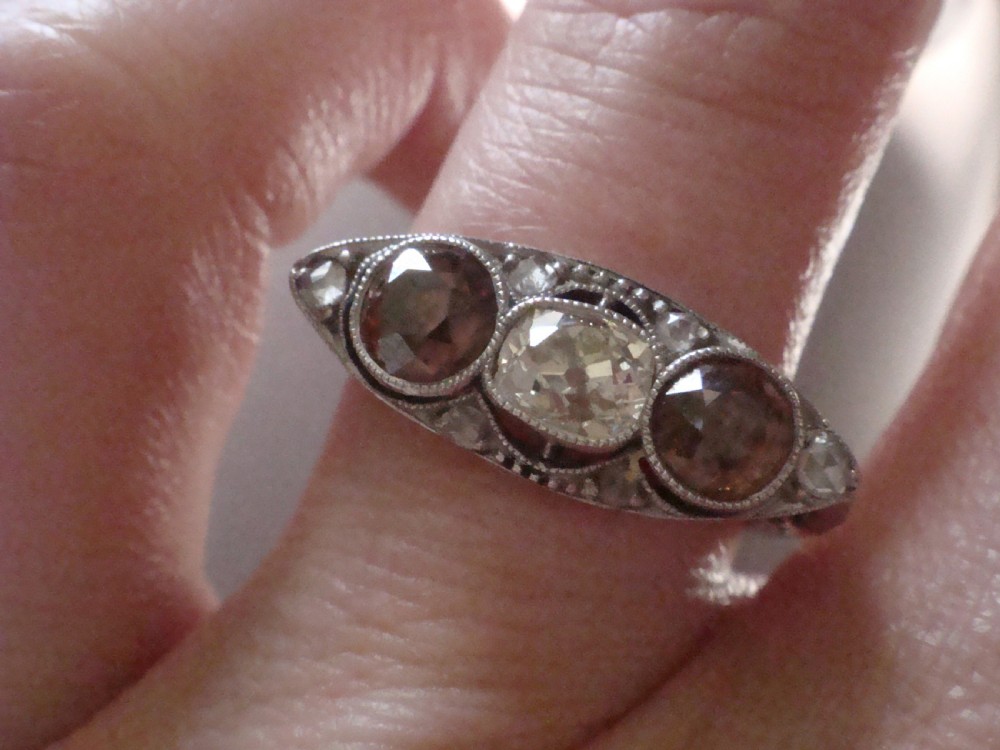 An antique platinum ring featuring a central round white diamond flanked by two natural brown diamonds with millegrain borders. View V