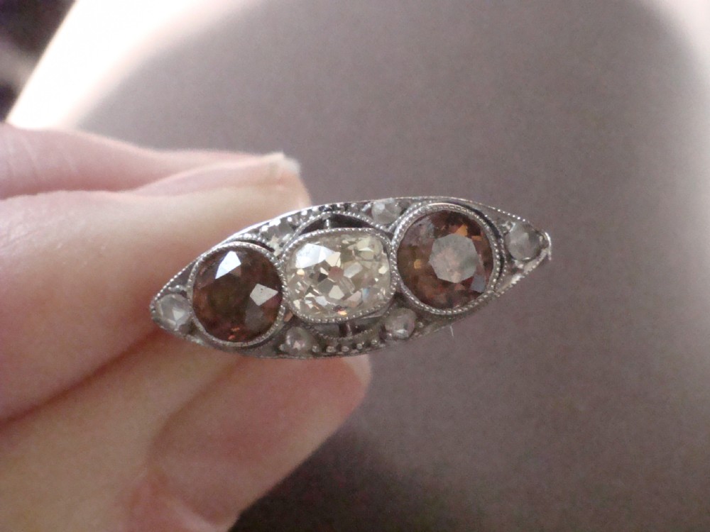 An antique platinum ring featuring a central round white diamond flanked by two natural brown diamonds with millegrain borders. View VI