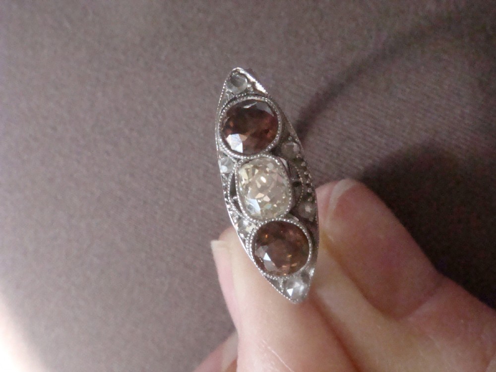 An antique platinum ring featuring a central round white diamond flanked by two natural brown diamonds with millegrain borders. View VII