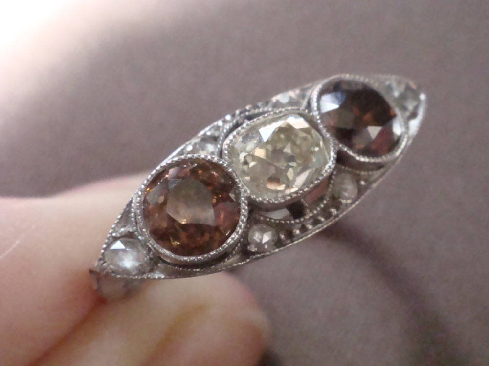 An antique platinum ring featuring a central round white diamond flanked by two natural brown diamonds with millegrain borders. View VIII
