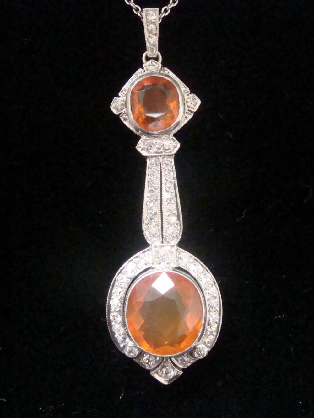 An Edwardian 18ct white gold pendant necklace featuring two oval cut orange fire opals framed by small diamonds along an articulated geometric drop. View III