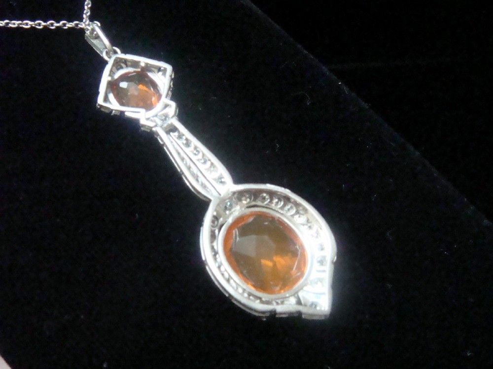An Edwardian 18ct white gold pendant necklace featuring two oval cut orange fire opals framed by small diamonds along an articulated geometric drop. View VII