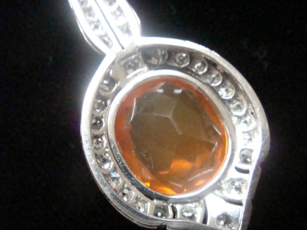 An Edwardian 18ct white gold pendant necklace featuring two oval cut orange fire opals framed by small diamonds along an articulated geometric drop. View VIII