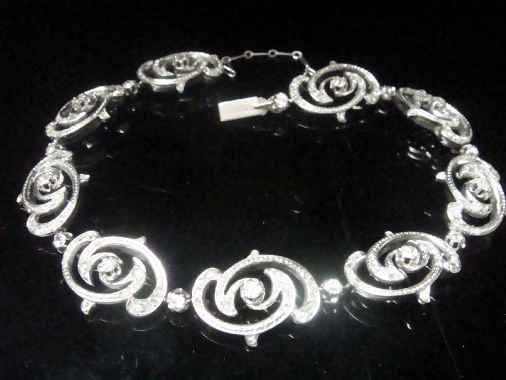 An antique platinum Art Nouveau bracelet featuring swirling openwork links set with diamonds and fitted with a safety chain.