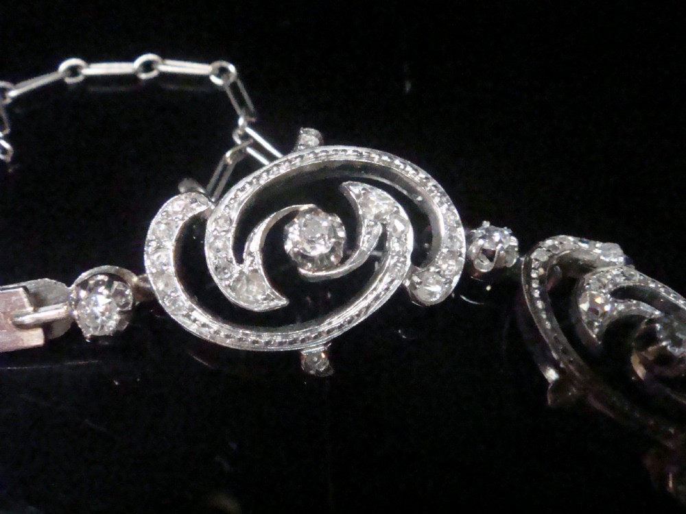 An antique platinum Art Nouveau bracelet featuring swirling openwork links set with diamonds and fitted with a safety chain. View II