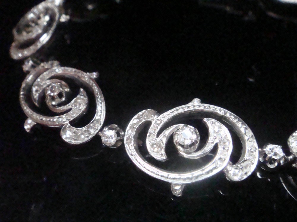 An antique platinum Art Nouveau bracelet featuring swirling openwork links set with diamonds and fitted with a safety chain. View III