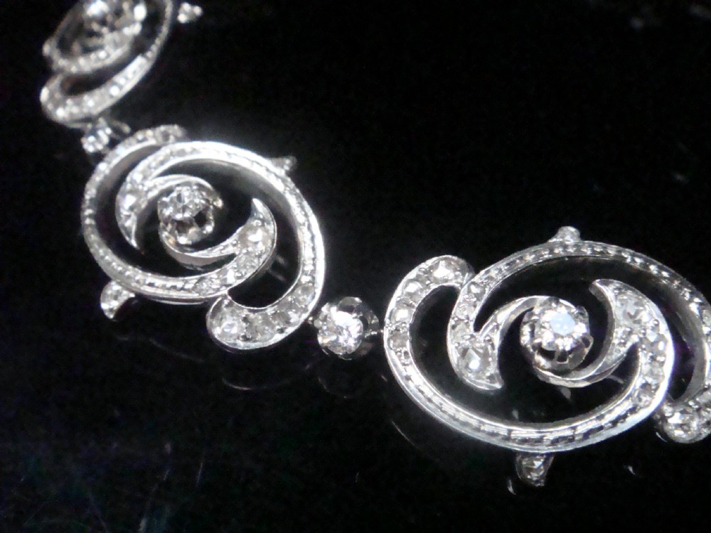 An antique platinum Art Nouveau bracelet featuring swirling openwork links set with diamonds and fitted with a safety chain. View IV