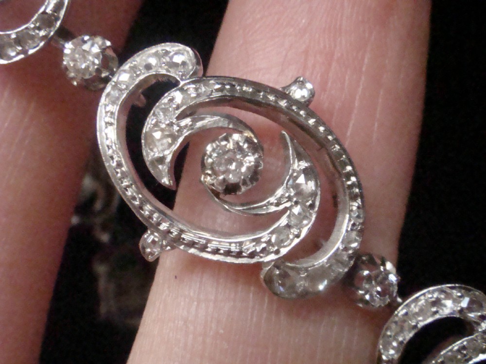 An antique platinum Art Nouveau bracelet featuring swirling openwork links set with diamonds and fitted with a safety chain. View V