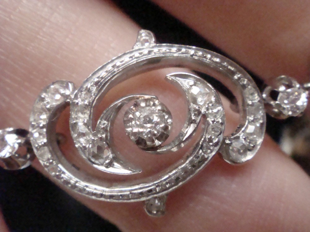 An antique platinum Art Nouveau bracelet featuring swirling openwork links set with diamonds and fitted with a safety chain. View VI