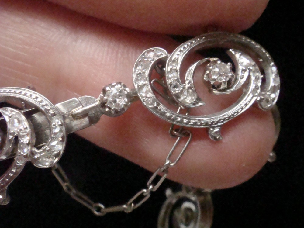 An antique platinum Art Nouveau bracelet featuring swirling openwork links set with diamonds and fitted with a safety chain. View VII