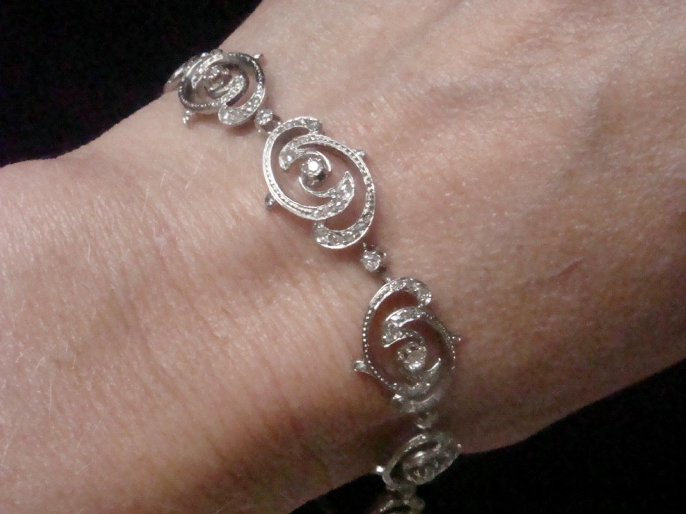 An antique platinum Art Nouveau bracelet featuring swirling openwork links set with diamonds and fitted with a safety chain. View VIII