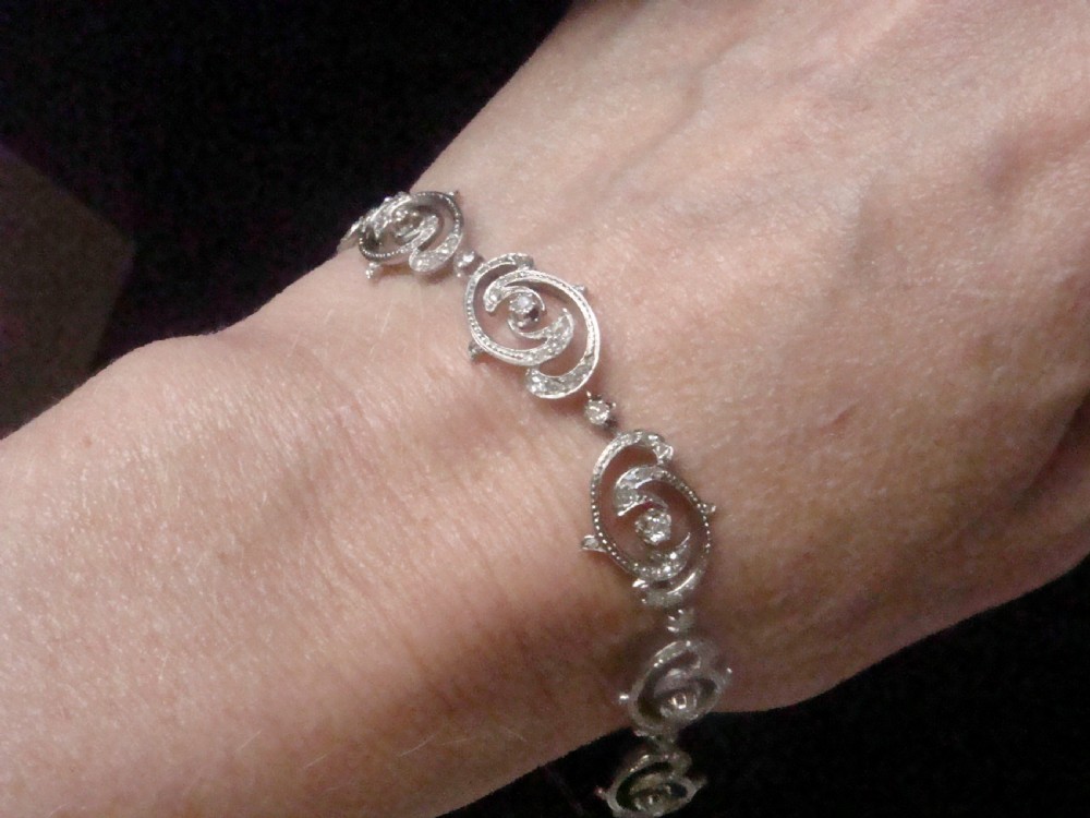 An antique platinum Art Nouveau bracelet featuring swirling openwork links set with diamonds and fitted with a safety chain. View IX