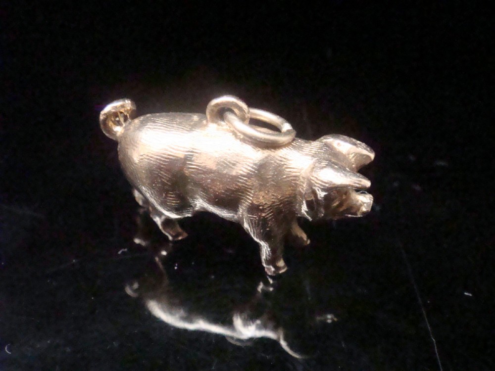 A small three-dimensional yellow gold pig pendant featuring a textured body, curled tail, and attached suspension loop.