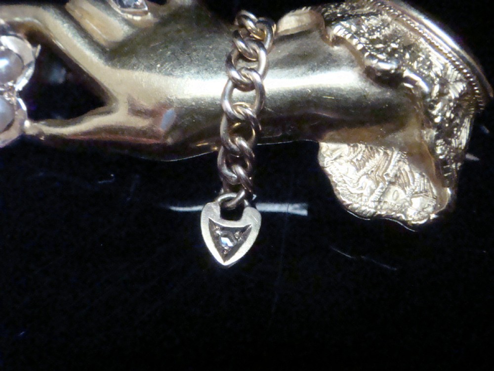 A Victorian 15ct yellow gold brooch carved in the shape of a hand with a lace cuff holding a seed pearl flower with a small heart padlock charm attached. View II