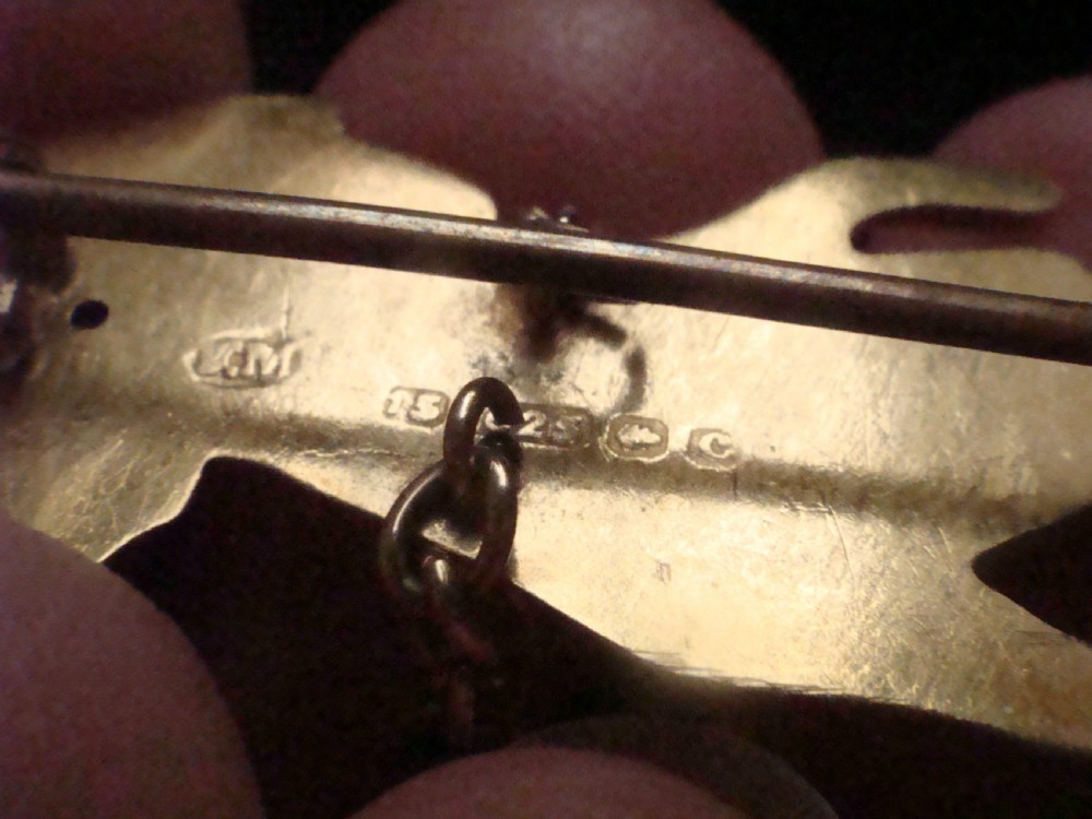 A Victorian 15ct yellow gold brooch carved in the shape of a hand with a lace cuff holding a seed pearl flower with a small heart padlock charm attached. View V