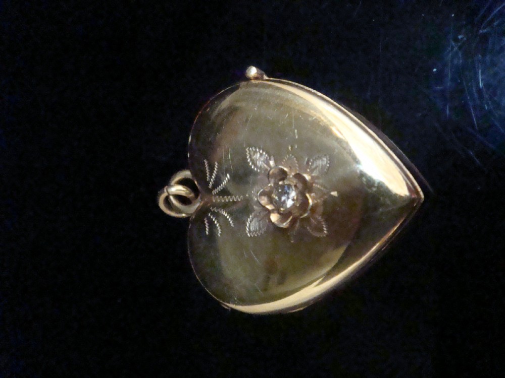 An antique gold heart-shaped locket featuring floral hand engraving and a central flush-set diamond. View II